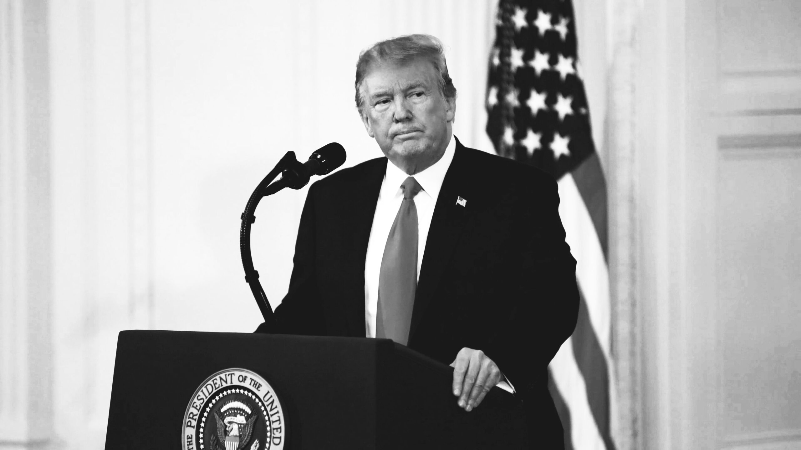 Donald Trump at a podium in black and white.