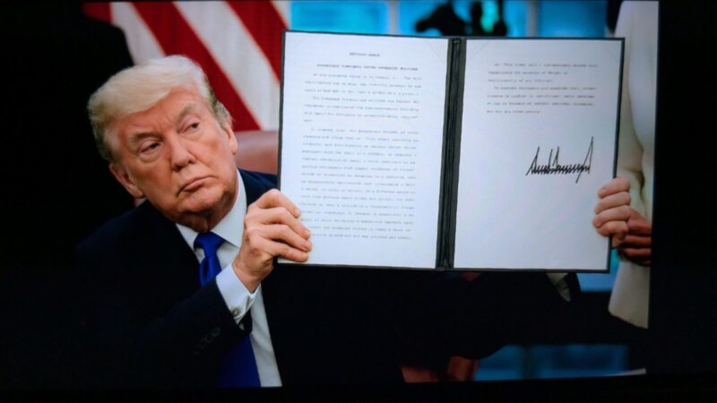 Donald Trump holding up an executive order in the Oval Office.