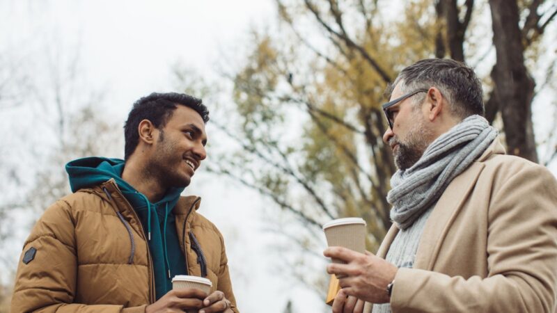 Two people talking to each other with coffees in their hands outside