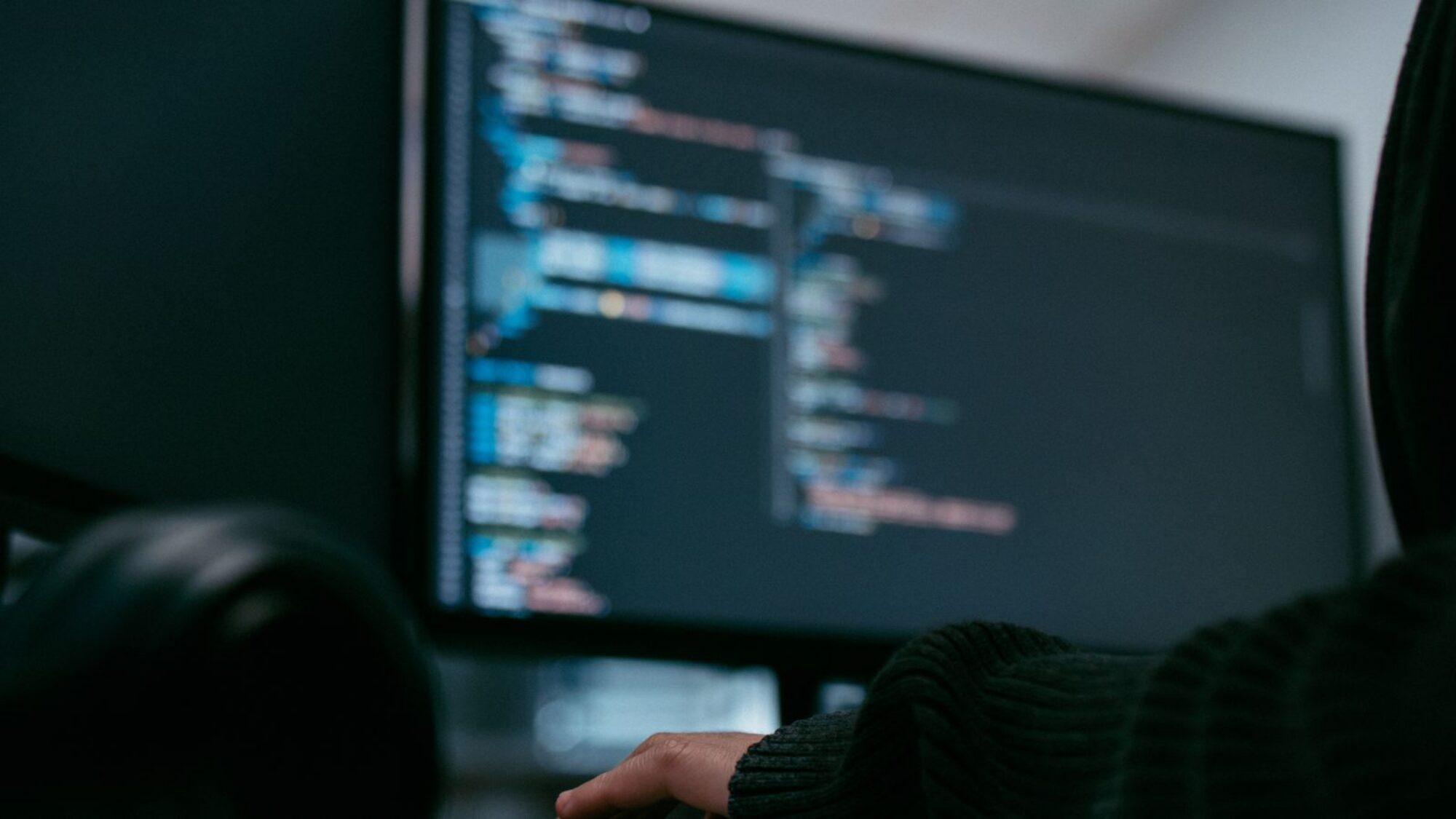 A hand on a keyboard with a screen in the background.