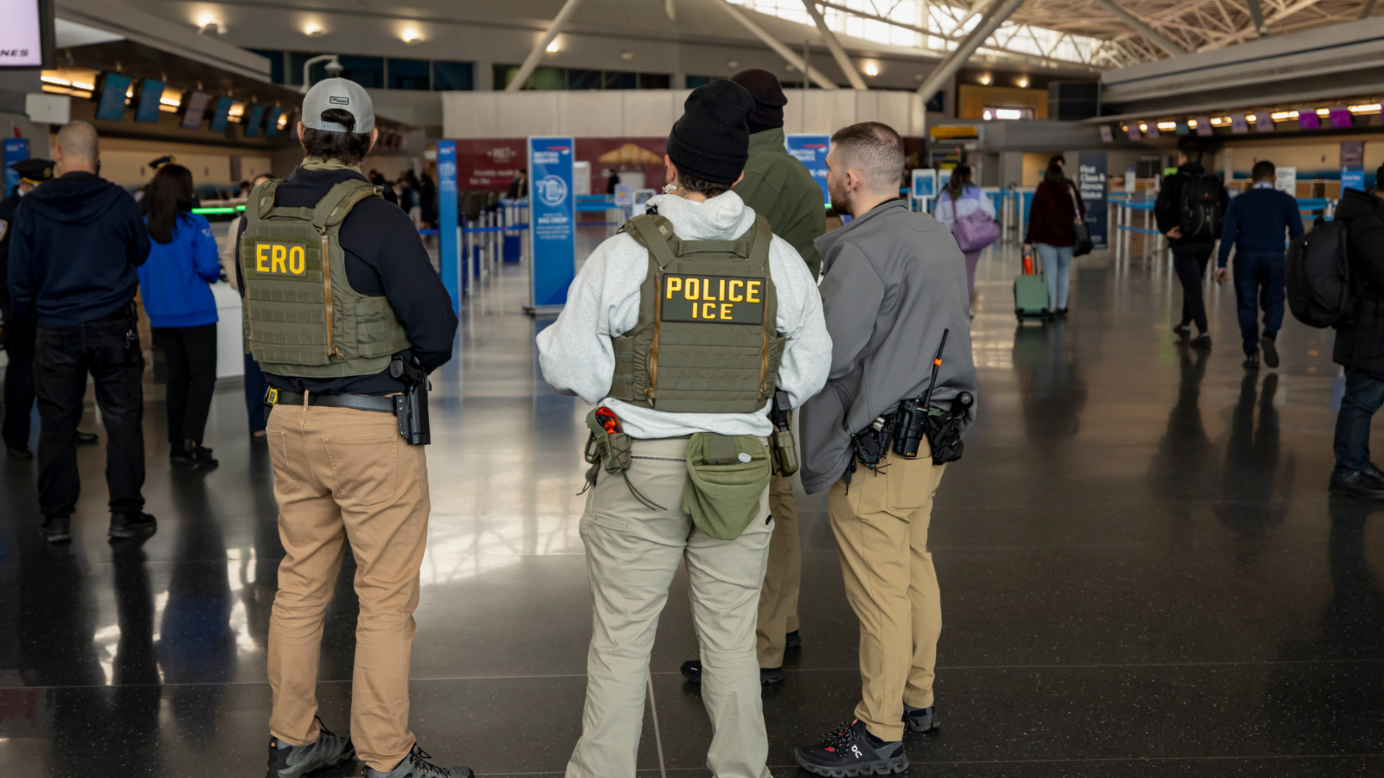 ICE agents in an airport with their backs turned