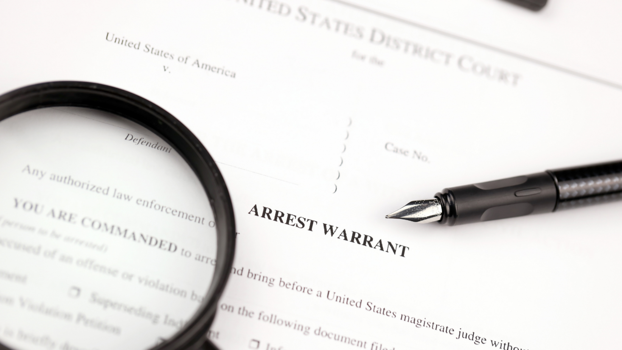 An arrest warrant with a pen and a magnifying glass on it.