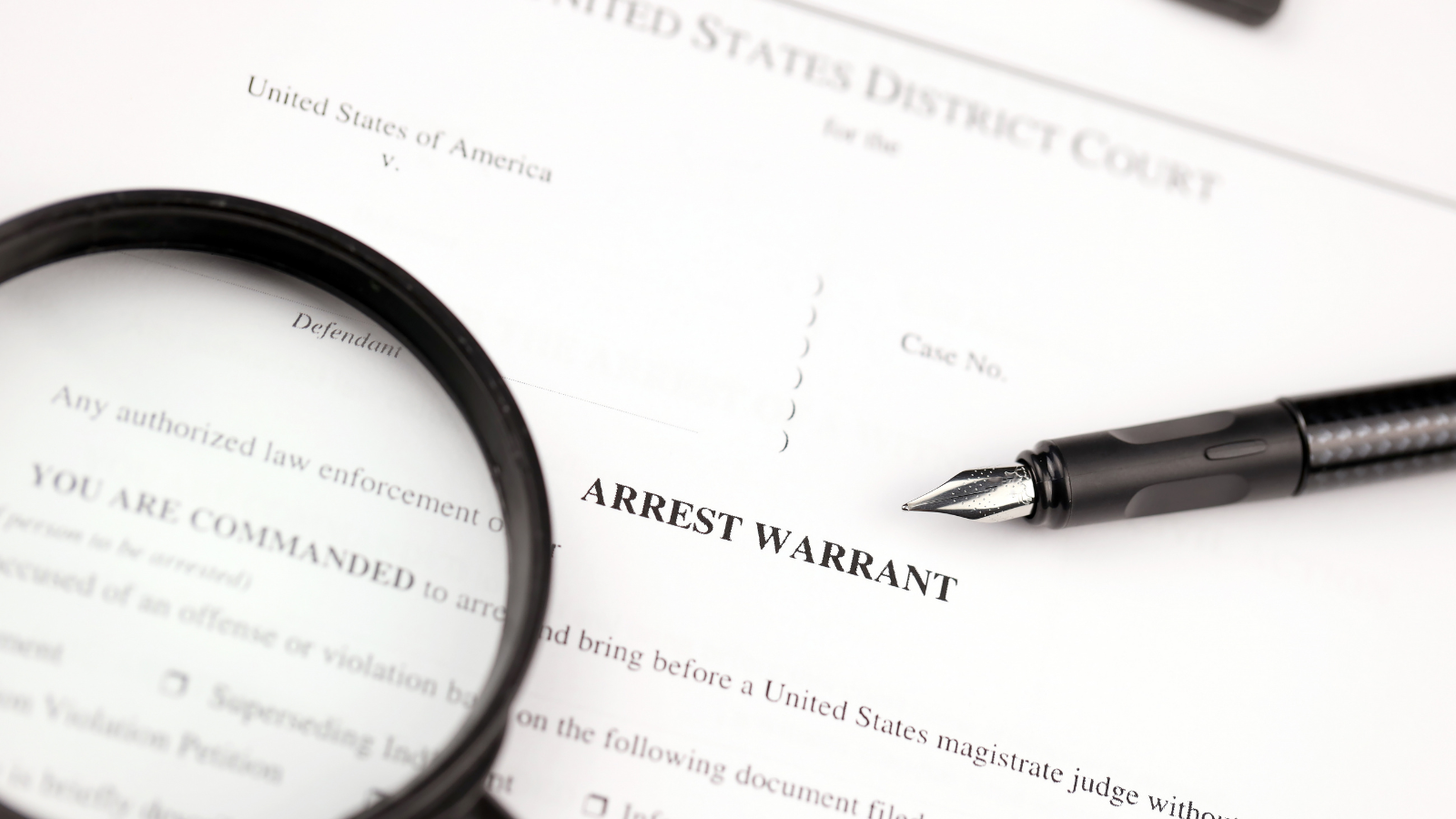An arrest warrant with a pen and a magnifying glass on it.