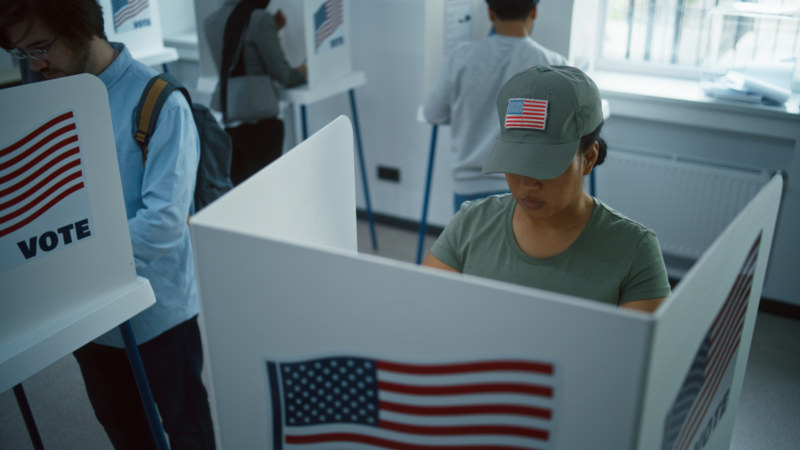 A person in a flag hat voting in a booth.